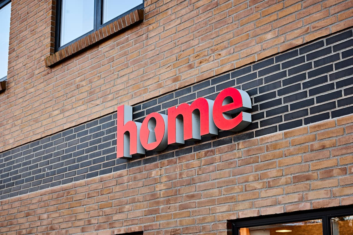 Rødt facadeskilt med home-logo på murstensfacade
