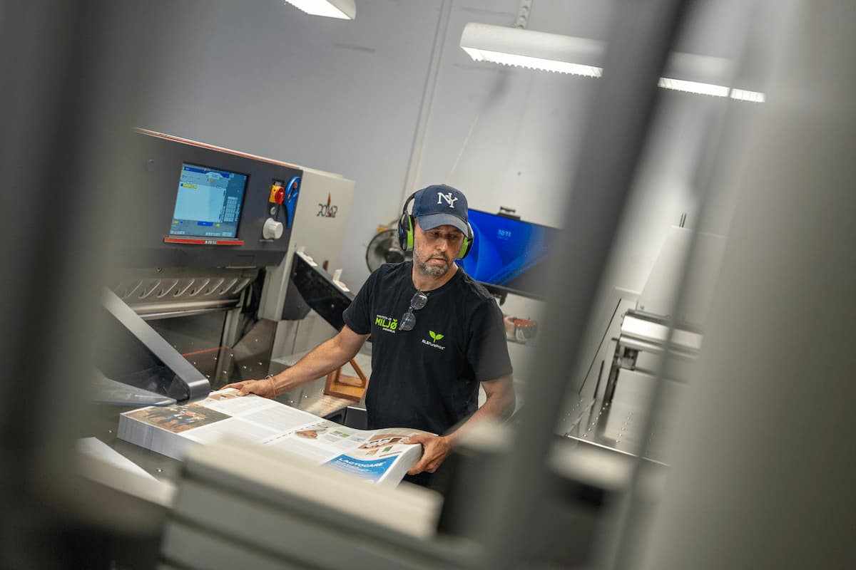 Medarbejder håndterer trykte ark ved en skæremaskine hos KLS PurePrint